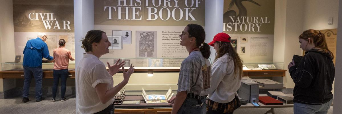 Students standing in front of an exhibit called history of the book while engaged in active discussion.